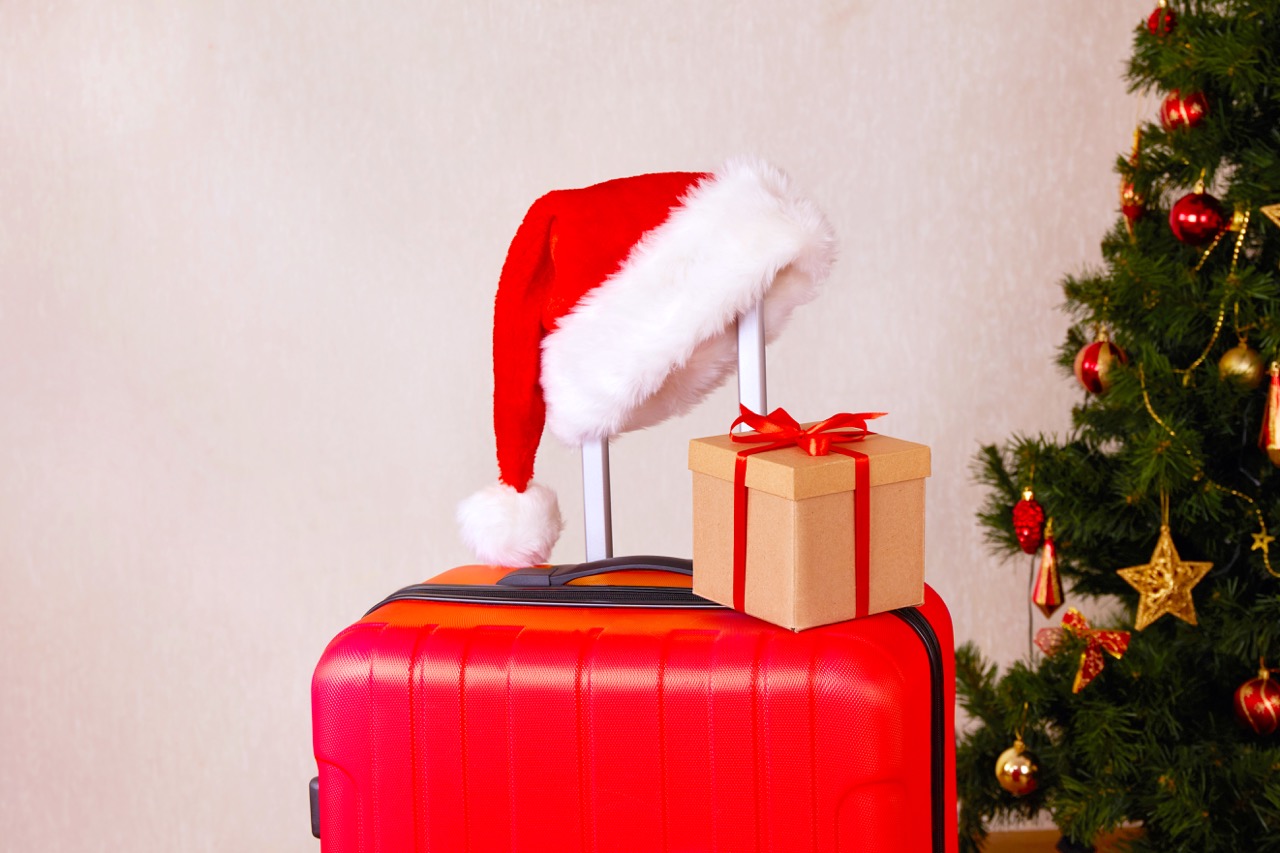 A red suitcase, a Santa Claus hat and a gift box. The concept of traveling for Christmas.