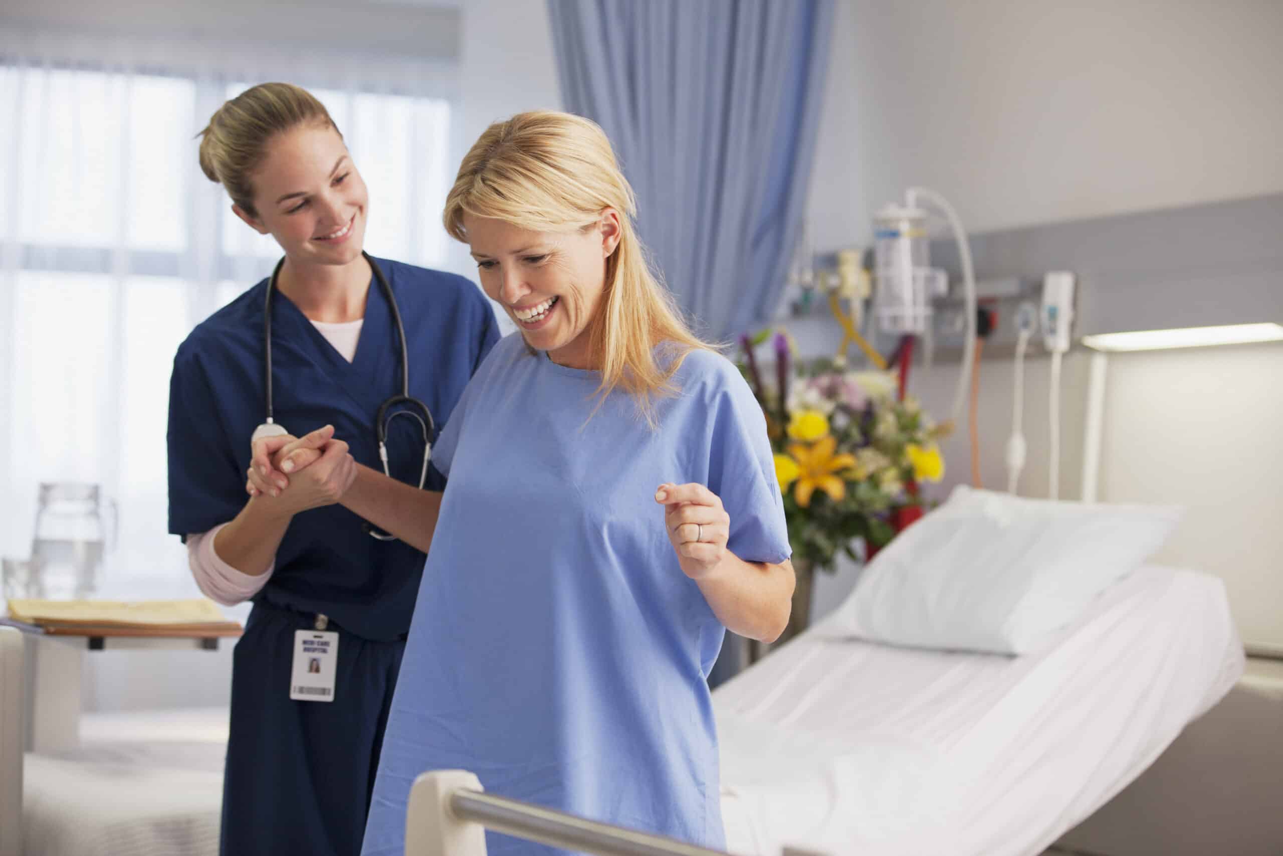 nurse helping happy patient stand in hospital room