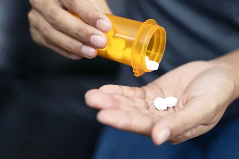 woman hand with pills on, spilling pills out of bottle on dark background